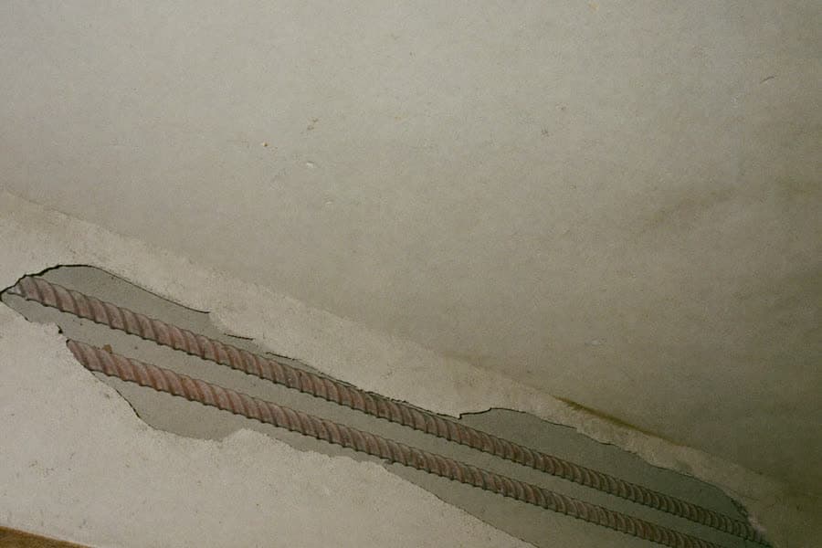 Abgestemmte Fehlstelle in der Untersicht einer Betonplatte: zwei Bewehrungsstäbe liegen auf ganzer Länge frei, ringsum steht der massive Beton mit sauberer Bruchkante an